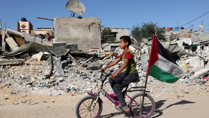 Un bambino in bicicletta di fronte alle macerie di un edificio distrutto a Gaza (afp)